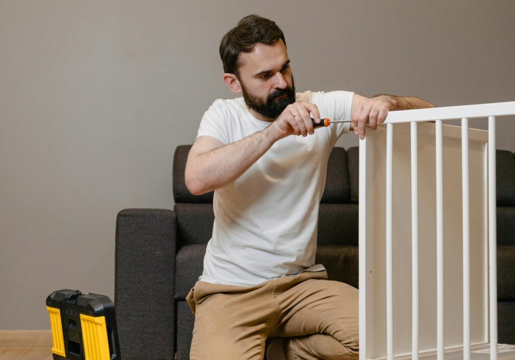 A father kneels beside a crib using tools, representing parenting and home life.