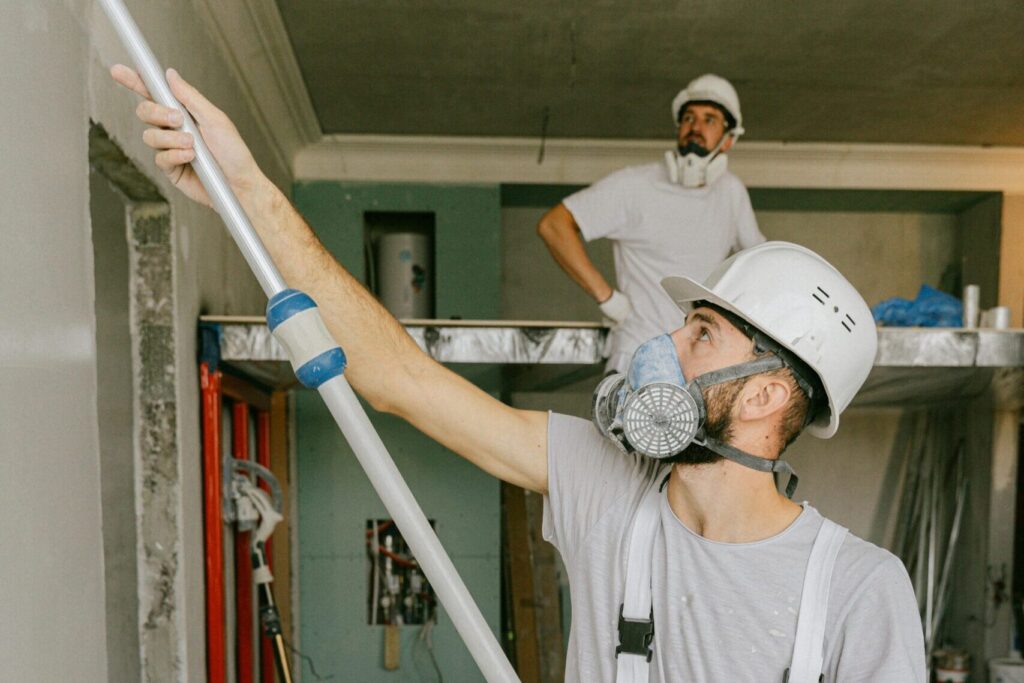 Two construction workers in safety gear are interior renovating, using a paint roller.